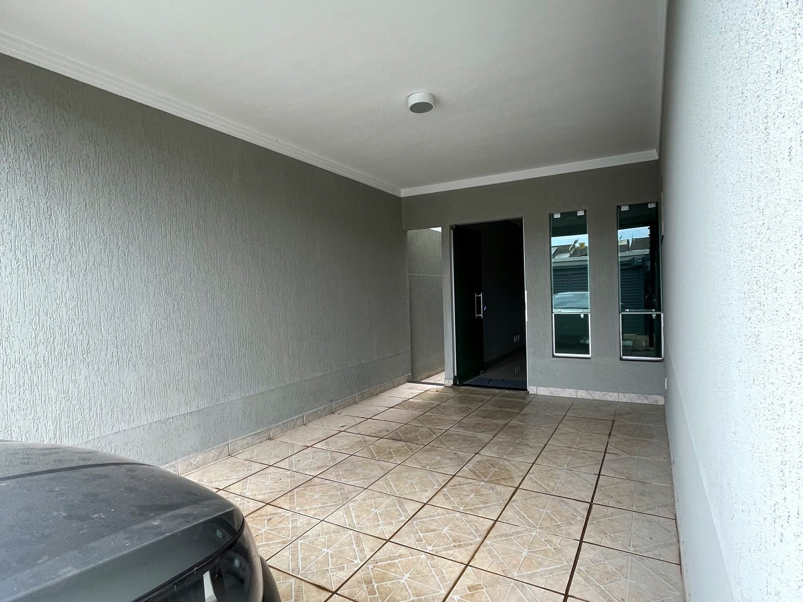Garagem coberta com piso cerâmico e entrada da casa ao fundo