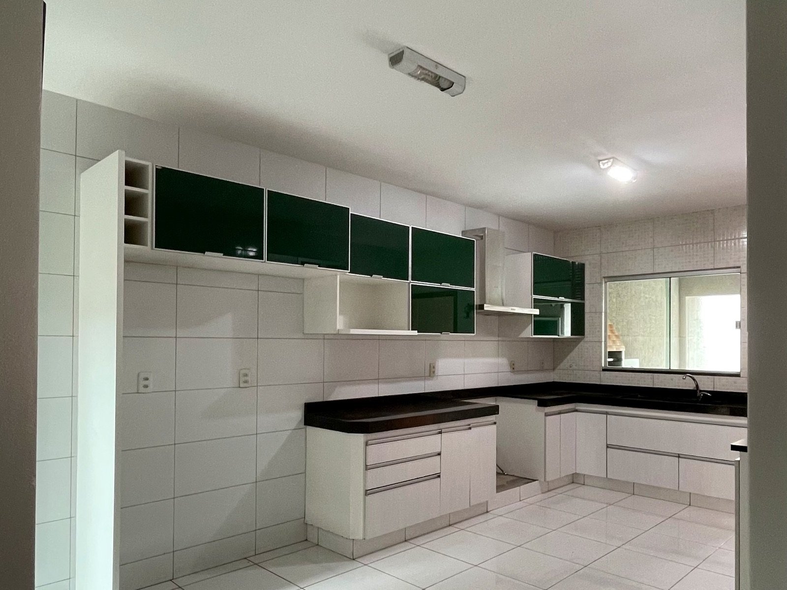 Cozinha em L com armários brancos e verdes e bancada de granito preto