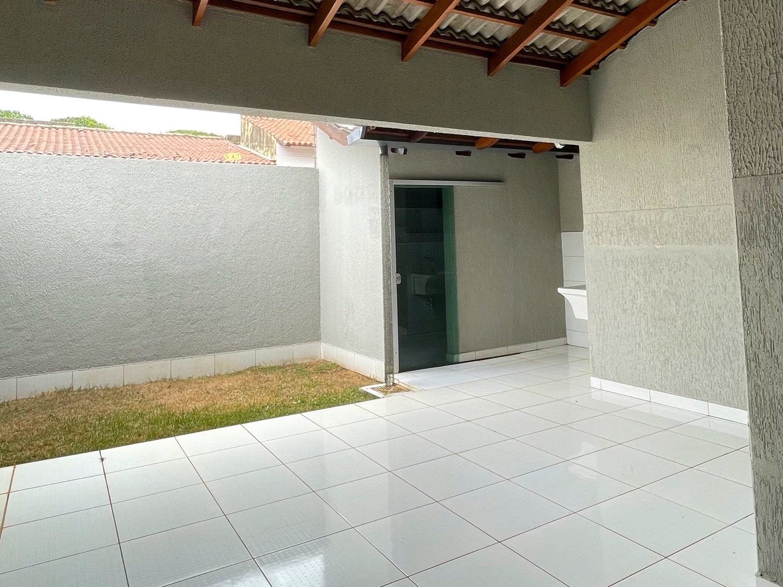A mesma área gourmet vazia, com piso branco, muro e faixa de grama